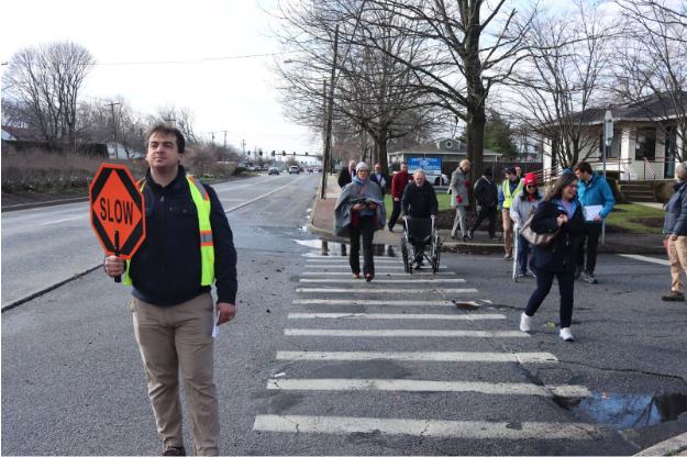 A man holds a stop sign at a crosswalk as several people cross behind him